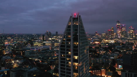 Dolly-shot-of-top-floor-of-modern-residential-building-in-Elephant-and-Castle-borough-against-night-city-panorama.-London,-UK