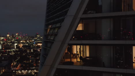 Night-ascending-footage-of-high-rise-luxury-apartment-building.-Revealing-city-panorama-with-glowing-windows-of-downtown-skyscrapers.-London,-UK