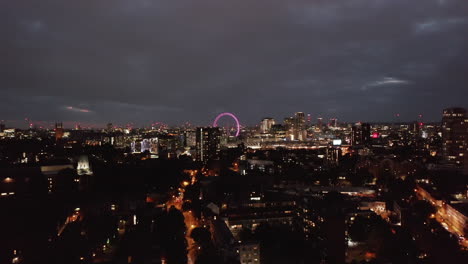 Descending-shot-of-night-cityscape.-Urban-neighbourhood-at-night.-Illuminated-London-Eye-in-distance.-London,-UK
