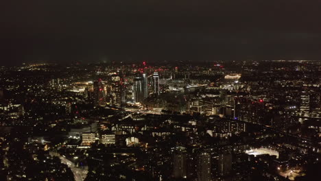 Aerial-panoramic-view-of-large-city-at-night.-City-lights-glowing-into-dark.-Fly-above-urban-neighbourhood.-London,-UK