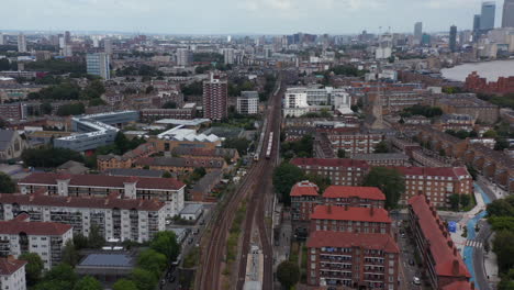 Forwards-tracking-of-trains-driving-side-by-side-on-railway-line-in-city.-Aerial-panoramic-view-of-urban-neighbourhood.-London,-UK