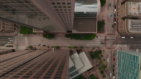 Aerial-birds-eye-overhead-top-down-view-of-wide-multi-lane-downtown-street-leading-between-tall-commercial-buildings.-Horizontally-panning-view.-Dallas,-Texas,-US