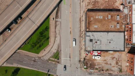 Aerial-birds-eye-overhead-top-down-tracking-view-of-white-van.-Car-driving-through-streets-of-neighbourhood,-under-highway-interchange.-Dallas,-Texas,-US