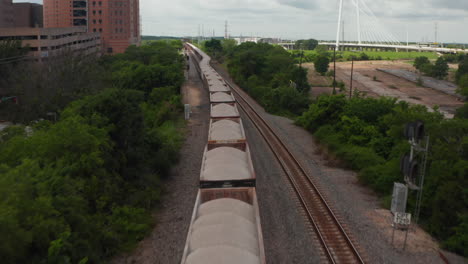 Aerial-view-of-long-train-standing-on-track.-Flying-over-freight-cars-with-dry-bulk-cargo.-Drone-following-railway.-Dallas,-Texas,-US