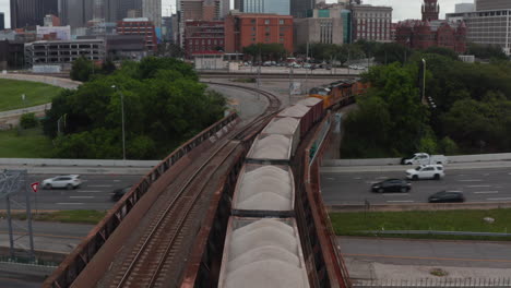 Forwards-reveal-of-freight-train-standing-on-track-leading-on-bridge-over-busy-highway.-Dallas,-Texas,-US