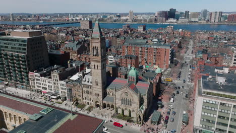 Aerial-descending-footage-of-old-stone-church-in-town-development.-Wide-flow-of-Charles-river-in-distance.-Boston,-USA