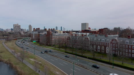 Busy-multilane-road-leading-on-waterfront-around-Harvard-university-complex.-Classical-red-brick-buildings.-Boston,-USA