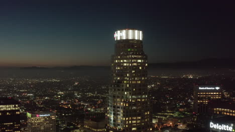 Famous-Skyscraper-US-Bank-Tower-of-Los-Angeles-Skyline-with-Rooftop-View-over-the-City-at-Night,-Aerial-Drone-Establishing-Wide-Shot,-Circa-2019