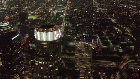 AERIAL:-Close-up-view-of-US-Bank-Tower-skyscraper-and-Downtown-Los-Angeles,-California-at-Night,-glowing-city-lights,-Circa-2019
