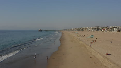 AERIAL:-People-at-the-Beach-Waves,Water-with-Pier-in-Los-Angeles,-California,-Sunny,-Blue-Sky