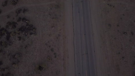 AERIAL:-Birds-view-of-lonely-abandoned-desert-road-with-red-car-driving-in-the-distance