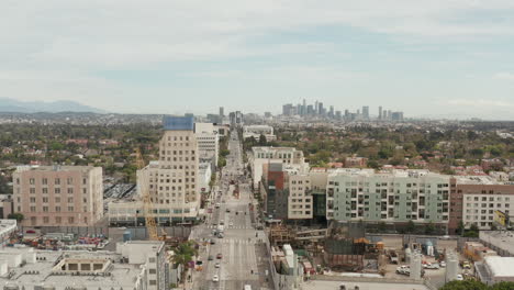 AERIAL:-Flight-over-Wilshire-Boulevard-towards-Downtown-Los-Angeles,-California-with-Constructions-Site-in-Foreground-on-Overcast-Day