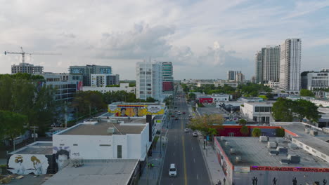 Aerial-descending-footage-of-town-development,-various-low-buildings-along-main-street-with-traffic.-Miami,-USA