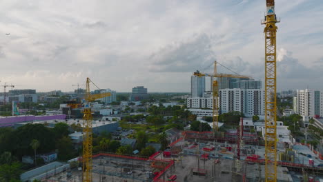 Forwards-fly-above-construction-site-with-machinery.-Group-of-yellow-cranes-helping-with-building-of-new-structure-in-city.-Miami,-USA