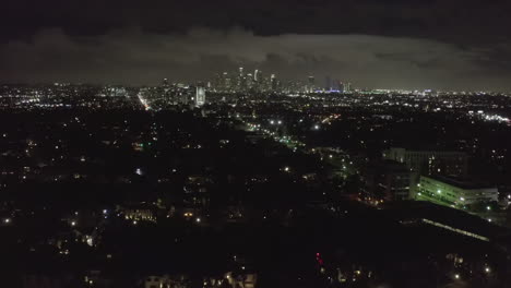 AERIAL:-Over-Dark-Hollywood-Los-Angeles-at-Night-with-Clouds-over-Downtown-and-City-Lights