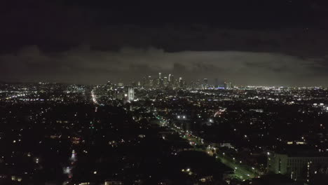 AERIAL:-Over-Dark-Hollywood-Los-Angeles-at-Night-with-Clouds-over-Downtown-and-City-Lights