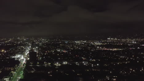 AERIAL:-Over-Dark-Hollywood-Los-Angeles-at-Night-view-on-Wilshire-Blvd-with-Clouds-over-Downtown-and-City-Lights
