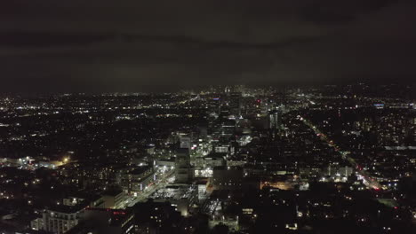 AERIAL:-Over-Dark-Hollywood-Los-Angeles-at-Night-with-view-on-Skyline-and-City-Lights