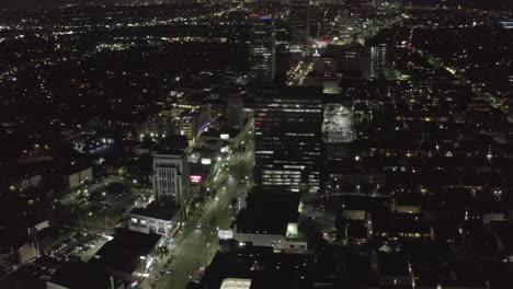 AERIAL:-Over-Wilshire-Boulevard-in-Hollywood-Los-Angeles-at-Night-with-Glowing-Streets-and-City-Car-Traffic-Lights