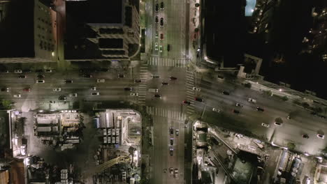 AERIAL:-Overhead-View-on-Intersection-Street-with-big-Construction-Site-and-Holes-in-Ground-at-Night-with-Glowing-Streets-and-City-Car-Traffic-Lights