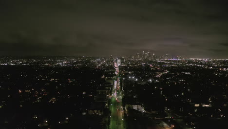 AERIAL:-View-over-Los-Angeles-at-Night-with-Wilshire-Boulevard-Glowing-Streets-and-City-Car-Traffic-Lights