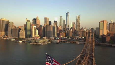 Luftbild:-Flug-über-Die-Brooklyn-Bridge-Mit-Amerikanischer-Fahnenschwingen-Und-Blick-Auf-Den-Ostfluss-über-Manhattan,-Die-Skyline-Von-New-York-In-Wunderschöner-Lage