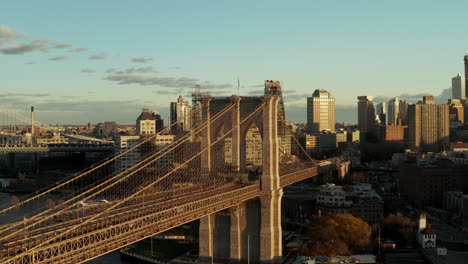 Forwards-ascending-fly-around-Brooklyn-Bridge-with-massive-stone-pillars-and-supporting-cables.-Urban-neighbourhood-in-background.-Brooklyn,-New-York-City,-USA
