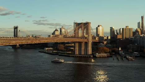 Passenger-cruise-ship-passing-under-Brooklyn-Bridge.-Fly-above-calm-river.-Urban-neighbourhood-in-background.-Brooklyn,-New-York-City,-USA