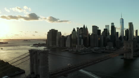 Fly-over-Brooklyn-Bridge-with-downtown-skyline.-Silhouettes-of-office-skyscrapers-against-sunset-sky.-Manhattan,-New-York-City,-USA