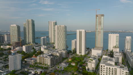 Forwards-fly-above-urban-borough.-Row-of-modern-tall-residential-buildings-on-waterfront-lit-by-bright-sunshine.-Miami,-USA