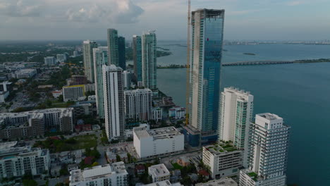 Slide-and-pan-footage-of-tall-apartment-buildings-on-bay-waterfront.-Aerial-view-after-sunset.-Miami,-USA