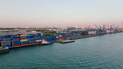 Slide-and-pan-shot-of-cargo-harbour-with-tons-of-naval-containers.-Buildings-lit-by-setting-sun-in-background.-Miami,-USA