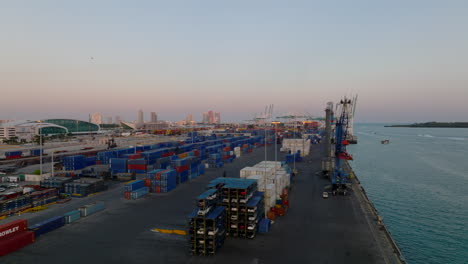 Slide-and-pan-footage-of-harbour-at-dusk.-Big-cranes-on-waterfront-and-rows-of-naval-containers-with-goods.-Miami,-USA