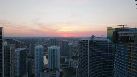Forwards-fly-above-modern-urban-borough.-Tall-residential-downtown-buildings-and-romantic-colourful-sunset-sky.-Miami,-USA