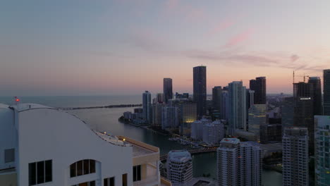 Group-of-tall-buildings-on-waterfront-at-dusk.-Backwards-reveal-of-residential-complex-of-luxury-high-rise-apartment-houses.-Miami,-USA
