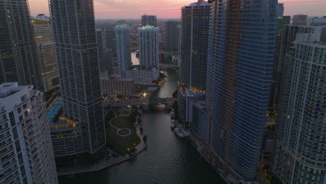 High-angle-view-of-river-flowing-through-modern-urban-borough.-Backwards-tilt-up-reveal-of-high-rise-apartment-buildings-at-dusk.-Miami,-USA
