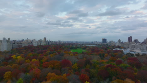 Forwards-fly-above-large-park-in-city-with-softball-fields.-Autumn-colourful-Central-park-lined-by-urban-neighbourhoods.-Manhattan,-New-York-City,-USA