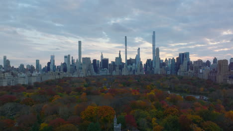 Wide-panoramic-view-of-skyscrapers-surrounding-Central-park.-Backwards-reveal-of-tourist-attractions-between-autumn-colour--trees.-Manhattan,-New-York-City,-USA