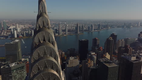 Fly-around-top-of-iconic-Chrysler-building.-Revealing-view-of-wide-East-river-and-boroughs-on-opposite-bank.-Manhattan,-New-York-City,-USA