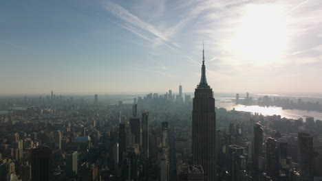 Forwards-fly-above-city.-Silhouette-of-iconic-Empire-State-Building-against-sun.-Hazy-view-of-cityscape.-Manhattan,-New-York-City,-USA