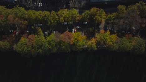 Aerial-birds-eye-overhead-top-down-view-of-piece-of-nature-in-city.-Fly-above-water-surface,-across-road-and-over-softball-fields-in-park.-Manhattan,-New-York-City,-USA